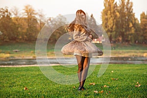 Happy stylish girl spinning at city park. Fashion and beauty. Luxury woman in trendy dress at sunset. Dream, carefree and