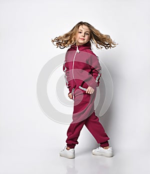 Happy stylish girl in a sports burgundy suit. a little schoolgirl stands with one hand in her pocket on a white