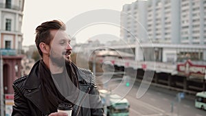 Happy stylish handsome man with a beard drinking takeaway coffee or tea looking to the side.