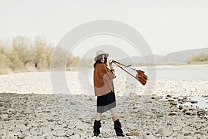 Happy stylish hipster traveler woman holding bag, in hat and fri