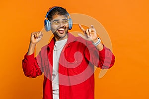 Happy stylish Indian man in sunglasses listening music via headphones, dancing disco having fun