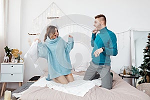 Happy stylish loving couple having a pillow fight in bed. young man and woman expecting baby for Christmas