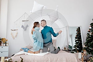 Happy stylish loving couple having a pillow fight in bed. young man and woman expecting baby for Christmas