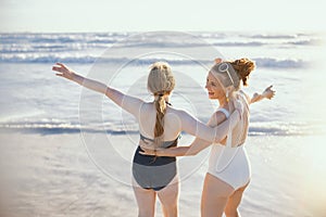 Happy stylish mother and teenage daughter at beach rejoicing