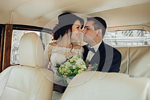 Happy stylish newlywed couple posing in retro car