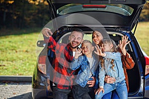 Happy stylish parents with their cute lovely children are making funny selfie on smart phone while sitting in the trunk