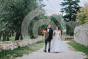 Happy stylish smiling couple walking in Tuscany, Italy on their wedding day. The bride and groom walk down the street by