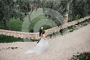 Happy stylish smiling couple walking in Tuscany, Italy on their wedding day. The bride and groom walk down the street by