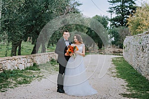 Happy stylish smiling couple walking in Tuscany, Italy on their wedding day. The bride and groom walk down the street by