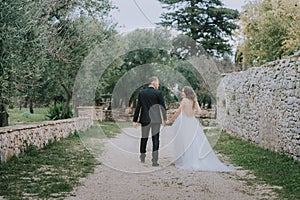 Happy stylish smiling couple walking in Tuscany, Italy on their wedding day. The bride and groom walk down the street by