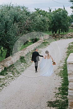 Happy stylish smiling couple walking in Tuscany, Italy on their wedding day. The bride and groom walk down the street by