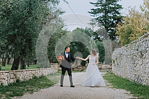 Happy stylish smiling couple walking in Tuscany, Italy on their wedding day. The bride and groom walk down the street by