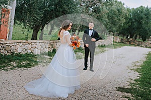 Happy stylish smiling couple walking in Tuscany, Italy on their wedding day. The bride and groom walk down the street by