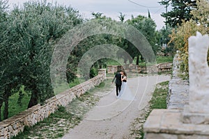 Happy stylish smiling couple walking in Tuscany, Italy on their wedding day. The bride and groom walk down the street by