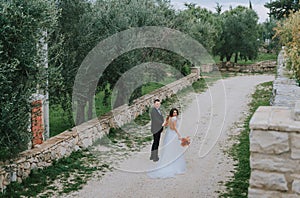 Happy stylish smiling couple walking in Tuscany, Italy on their wedding day. The bride and groom walk down the street by