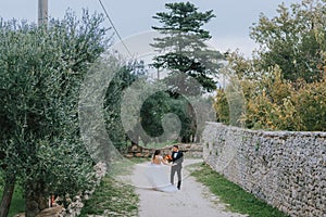 Happy stylish smiling couple walking in Tuscany, Italy on their wedding day. The bride and groom walk down the street by