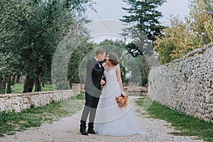 Happy stylish smiling couple walking in Tuscany, Italy on their wedding day. The bride and groom walk down the street by