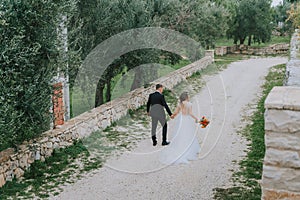 Happy stylish smiling couple walking in Tuscany, Italy on their wedding day. The bride and groom walk down the street by