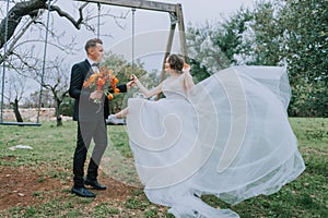 Happy stylish smiling couple walking in Tuscany, Italy on their wedding day. Newlyweds with the swing in the park. The