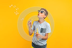 Happy stylish teen guy blows soap bubbles on an yellow background