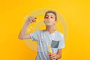 Happy stylish teen guy blows soap bubbles on an yellow background