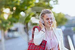 happy stylish woman in city listening to music with headphones