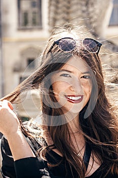 happy stylish woman with gorgeous smile and hair, posing in sunlight in city street. beautiful hipster girl in fashionable outfit