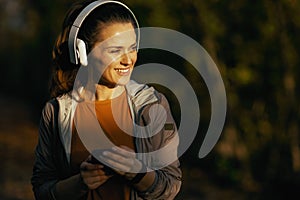 happy stylish woman in park listening to music with headphones