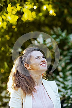 happy stylish woman in pink dress and white jacket in city