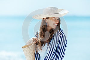 happy stylish woman on seashore with straw bag