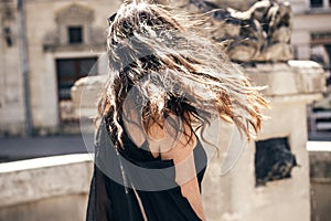 Happy stylish woman waving hair in sunlight at old european city