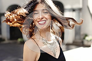 Happy stylish woman waving hair in sunlight at old european city