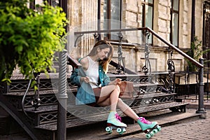 Happy stylish young woman with vintage roller skates and bag sitting on stairs