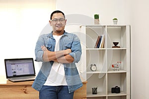 Happy succesful young Asian entrepreneur smiling at camera confidently in his home office studio