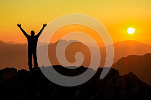 Happy success winning man arms up on mountain at sunset