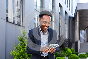 Happy successful African American businessman counts, waves, throws, show off, flaunt, cash money background a modern office