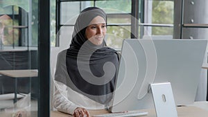Happy successful arab businesswoman in hijab typing on keyboard working on computer enjoying work online in modern