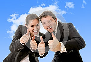 Happy successful business Hispanic woman and Caucasian man wearing suits giving thumbs up smiling on blue sky