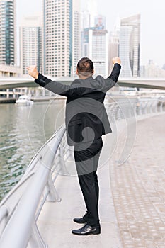 Happy successful business man celebrate win with raised arms with skyscrapers in the background