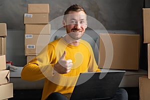 Happy successful business man thumb up working with laptop and cardboard box in home office. online business success