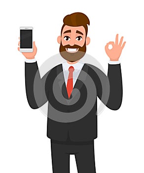 Happy successful businessman showing smart phone, mobile, cell phone in hand and gesturing okay or OK sign. Good, deal, agree.