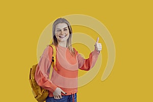 Happy successful student girl standing on yellow background, showing thumbs up and smiling