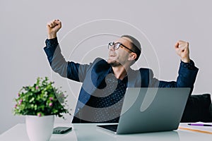 Happy successful young business man cheering with clenched fists in office