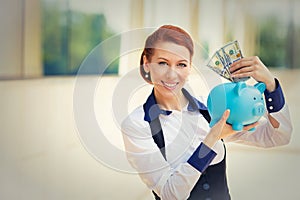 Happy successful young business woman depositing money dollars in piggy bank