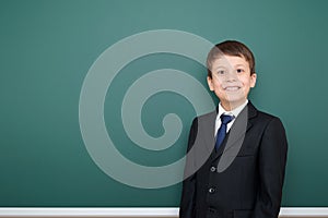 Happy successfull school boy in black suit portrait on green chalkboard background, education concept