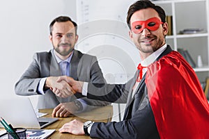 happy super businessman in mask and cape shaking hands with businessman