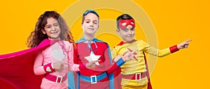 Happy superhero kids pointing away in studio