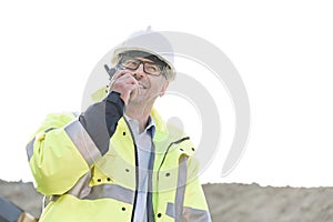 Happy supervisor using walkie-talkie at construction site against clear sky