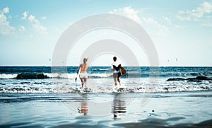 Happy surfer couple going to surf - Sporty people having fun surfing in the ocean