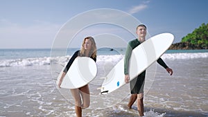 Happy surfers couple in love coming out of ocean waves satisfied with their surf session. Cheerful boy and girl walking